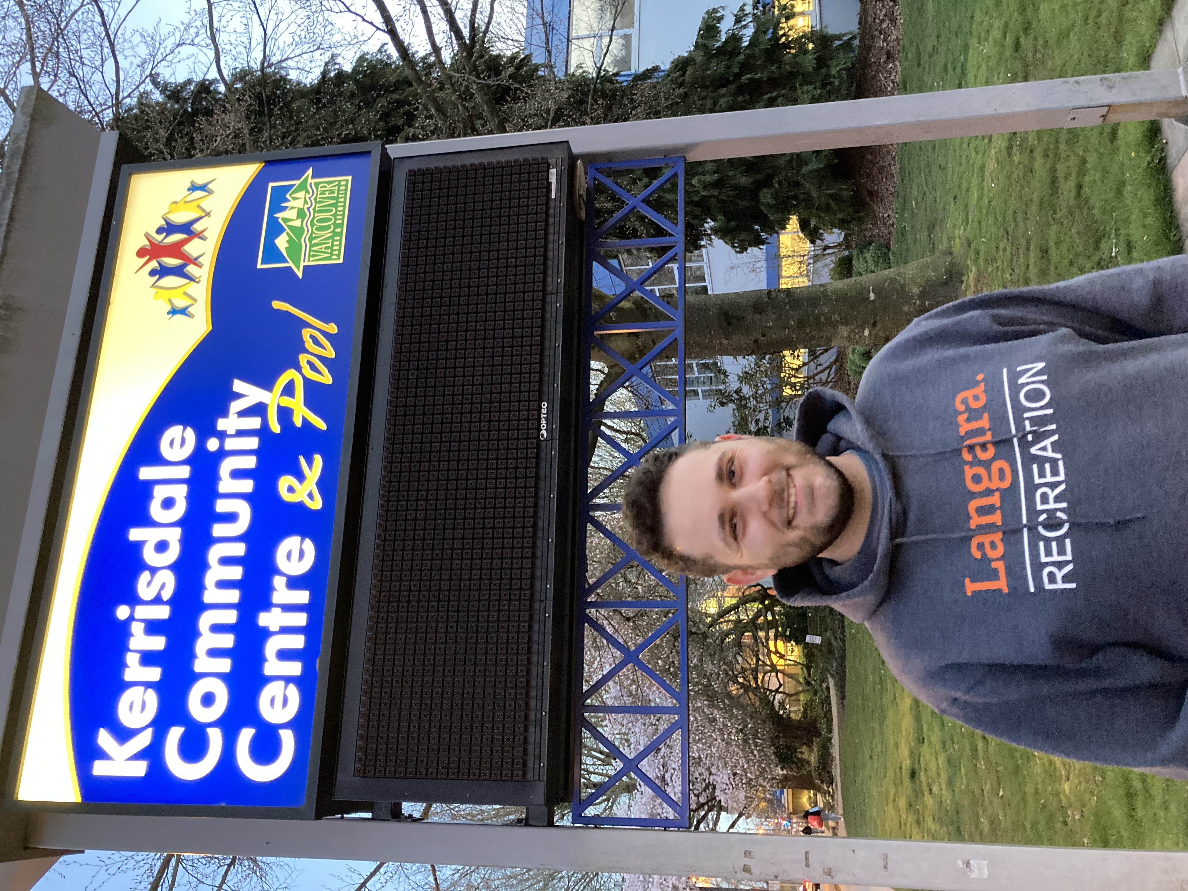 Man smiling below a sign that reads Kerrisdale Community Centre & Pool